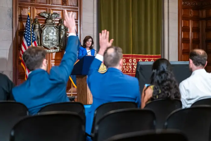 Reporters raise their hands to ask Gov. Kathy Hochul a question at a press briefing.